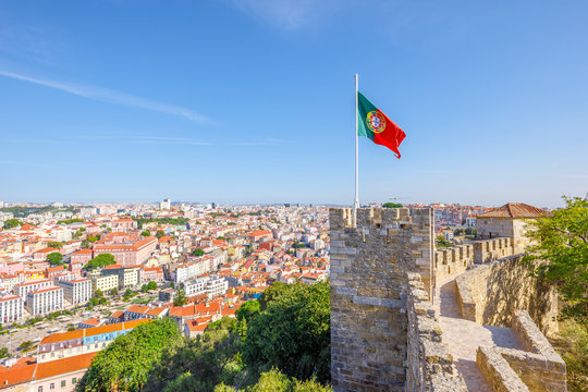 Lisbon aerial view cityscape with Portugal flag waving on ancient fortress wall of Sao Jorge Castle, at Moorish castle on highest hill in Alfama. Lisbon Castle is a popular tourist attraction.