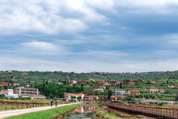 Southern village tiny people cycling by the water water channel tiny red roof houses on the hill Adriatic Slovenia Europe
