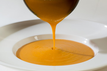 Vegetable soup being poured into a white dish