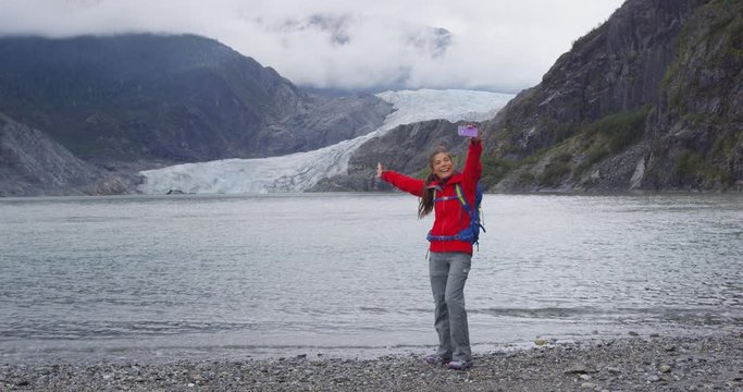 Tourist in Alaska taking selfie video by glacier or having fun making funny social media post. Woman tourist on smart phone on travel vacation by beautiful Mendenhall Glacier landscape.
