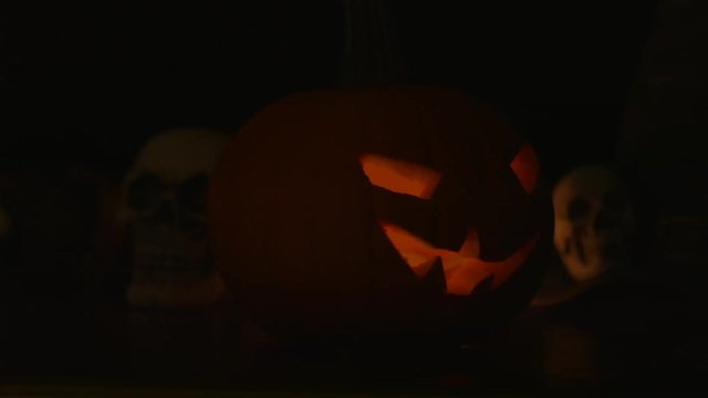 Carved Halloween pumpkin lights inside with flame and skuls around.