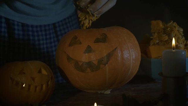 Male hands scooping out seeds and contents of pumpkin on wooden table with candles at night. Halloween theme, jack lantern