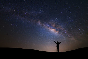 Fototapeta premium Landscape with milky way galaxy and space dust in the universe, Night sky with stars and silhouette of a standing sporty man with raised up arms on high mountain.