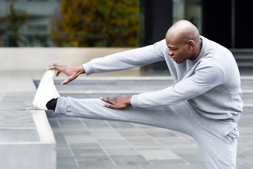 Black man doing stretching before running in urban background