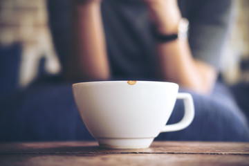 Closeup image of a woman sitting in cafe with white ceramics cup of hot coffee on vintage wooden table in cafe