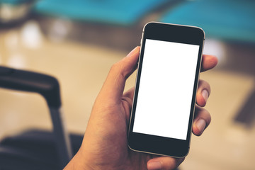 Mockup image of a man's hand holding and using black mobile phone with blank white screen with black baggage in airport