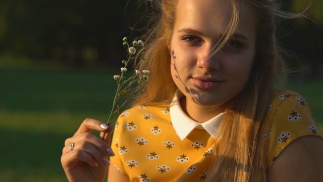 Slow motion Young blond girl in european style in a warm sunny day in a meadow in the park. the girl is dressed in a bright yellow dress in flowers. green grass, sunny day. The girl is holding a small