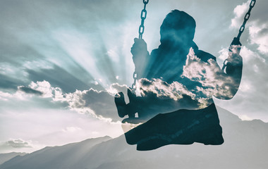 Double exposure of kid on swing and gorgeous cloudscape