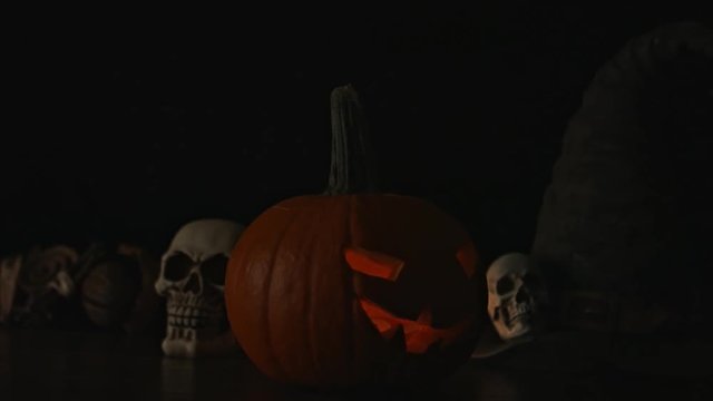 Carved Halloween pumpkin lights inside with flame and skuls around.