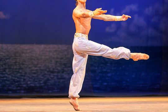 dancing, rehearsal, amusement concept. on the stage of theater man wearing light blue pants and pointe shoes performing the dance solo of well known great ballet corsar
