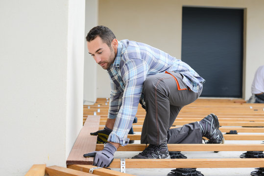 handsome young man carpenter installing a wood floor outdoor terrace in new house construction site