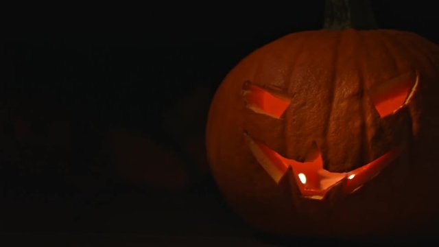 Carved Halloween pumpkin lights inside with flame and skuls around.