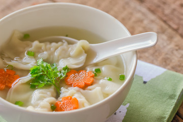 Close up minced pork wonton soup in white bowl on napkin put on wood table. Homemade delicious wonton in clear soup for breakfast or lunch or dinner.Wonton soup is always popular Chinese food.