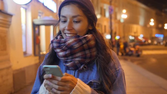 Smiling Caucasian Girl Texting on Mobile Phone and Walking on Streets of Night Saint Petersburg. 4K, Slowmotion. Russia.