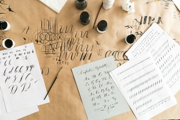 lettering, creation, work concept. paper with linens for training skills in calligraphy, black and white inks, brushes with thin tips and beautiful letters of english alphabeth written by designer