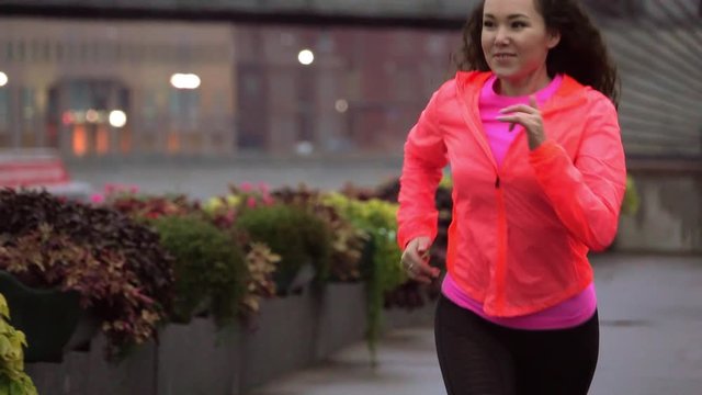 Cheerful mixed race woman starts running along city park embankment in the evening, slow motion