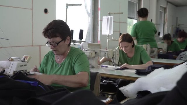 Portrait of mature female dressmaker during sits for the sewing machine and tailoring, group of woman working in the blurred background, steady cam,room interior