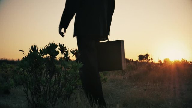 Business man in elegant suit walks on top of a mountain at sunset