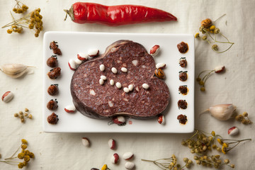 Black pudding on square white plate with kidney bean, chili pepper and garlic on white tablecloth