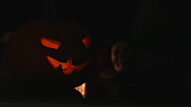Carved Halloween pumpkin lights inside with flame and skuls around.