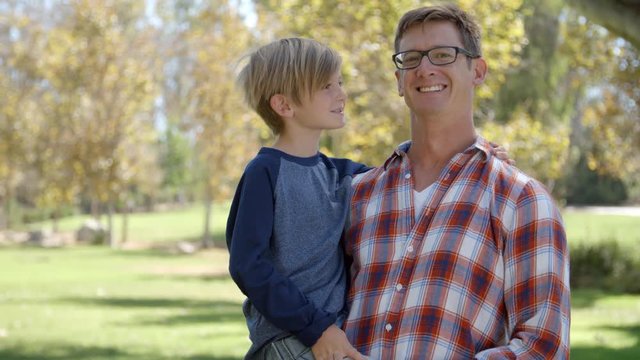 Father carrying seven year old son smiles to camera in park