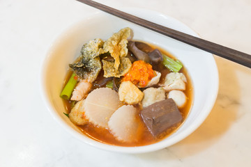 Red sauce noodle soup with flat rice noodles fish balls, fish long sliced, crispy squid and crispy fish skin.
