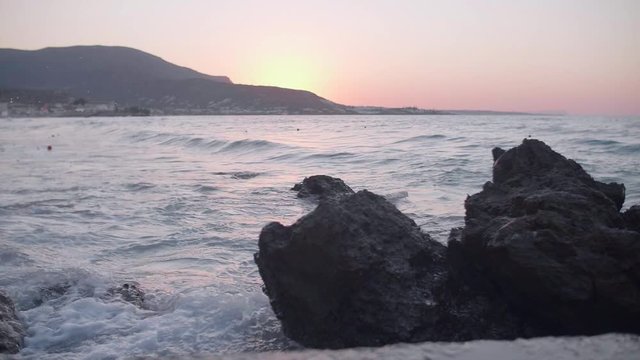 Beautiful dramatic skies and amazing sunrise over the beach in Creete, Greece. Mediterranean sea waves crash into rocks at dusk in slow motion.