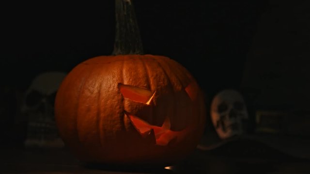 Carved Halloween pumpkin lights inside with flame and skuls around.