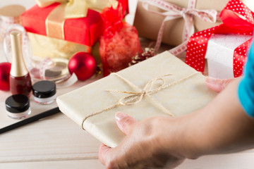 Female hands are wrapping cosmetics in christmas gifts on white wooden background
