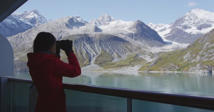 Tourist looking at Alaska Glacier Bay landscape using binoculars on cruise ship. Woman on vacation travel looking for wildlife enjoying cruising famous tourist destination. RED EPIC SLOW MOTION.