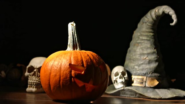 Carved Halloween pumpkin lights inside with flame and skuls around.