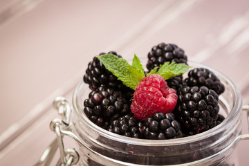 Red raspberries and blackberries in a glass jar with a leaf of mint