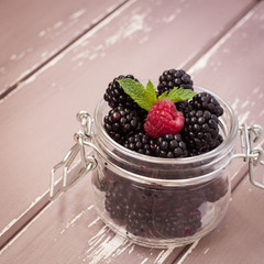 Red raspberries and blackberries in a glass jar with a leaf of mint, 1x1 size