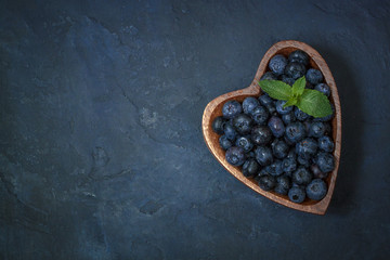 Fresh blueberries with a leaf of mint in the heart-shaped bowl, flat