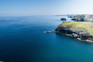 An aerial view from clifftops looking out to the horizon of a deep, blue, calm ocean at Tintagel in Cornwall, UK which is the seat of the legendary English King Arthur and shows cliffs.