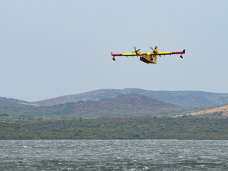 Fototapeta na wymiar Firefighter airplane, water bomber, air tank taking water from the sea and extinguishing forest fire in Croatia, close to Krka national park and Skradin town, Sibenik region
