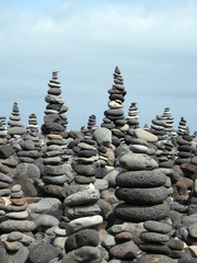 rock art piles and towers of grey stones and pebbles on a beach with blue sky