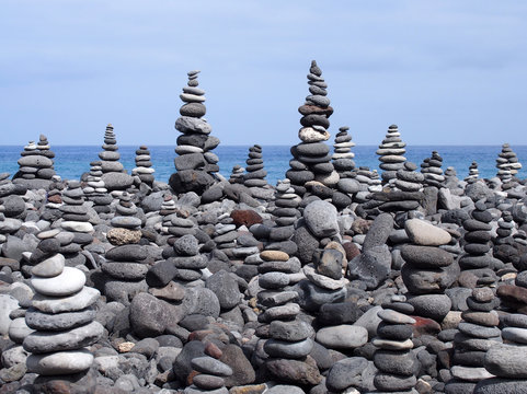 rock art piles and towers of grey stones and pebbles on a beach with blue sky and blue sky