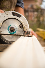 worker saws a wooden plank at a construction site