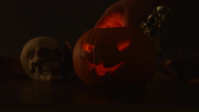 Carved Halloween pumpkin lights inside with flame and skuls around.