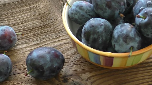 A bowl of ripe blue plums on a dark wooden background
