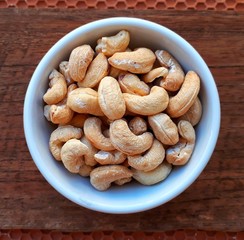 Closeup top view the white bowl of dry cashew nut on wooden background, selective focus.  