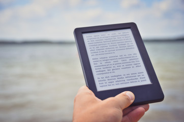 Hand holding electronic reader on the background of sea waves. Lorem ipsum text used. Toned image.