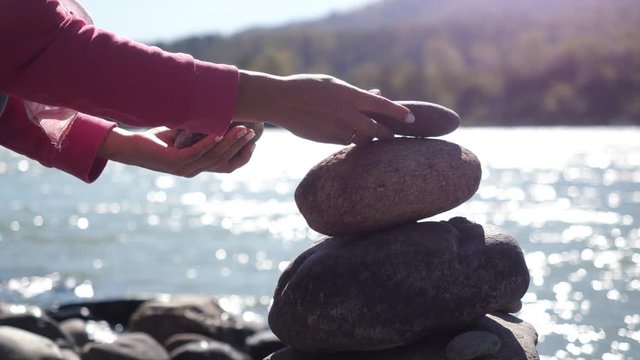 Female hands putting pebble stack next to the mountain river in slow motion. 3840x2160