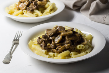 Supper plates with thick creamy mushroom and beef stroganoff on pasta and rustic white background