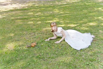 Bride in white lying on grass next to the squirrel