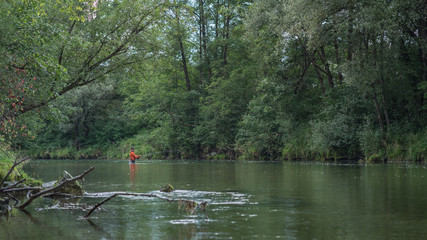 Angler mit Wathose und Watjacke im Wasser beim Angeln mit Fliegenrute bei Regen im klaren Fluss stehend und werfend