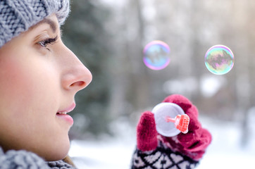 Young beautiful woman blowing bubbles in winter clothing outdoors. Focus on lips. Soap bubbles.