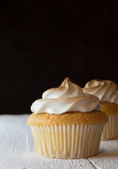 Cup cake with egg white meringue topping on white wooden table and one defocused against a dark bacground.
