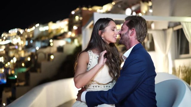 4k travel video rich honeymoon couple in love in beautiful clothes kissing outdoors on terrace of luxury hotel in santorini on romantic evening